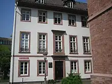 Photograph of a three-story white house with large windows framed with red sandstone