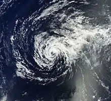 A satellite image depicts the tropical cyclone over the open waters as a spiral of patchy low-level clouds, devoid of strong thunderstorms.