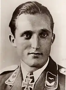 The head and shoulders of a young man, shown in semi-profile. He wears a military uniform with an Iron Cross displayed at the front of his white shirt collar.