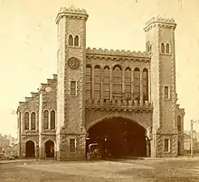 A castle-like railway station with a broad arch over the two tracks