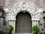 Ornate side portal, featuring pink reliefs of the Visitation at the top, and figures of Saint Zachary (vested as a kohen) and Saint Elizabeth to the sides