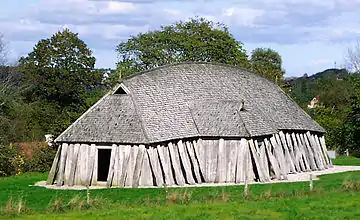 A primitive one-storey hut made of wooden planks with shingled roof, a single entrance and a few small skylights.