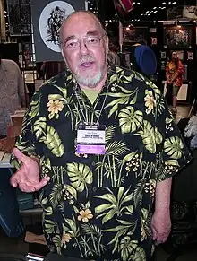 A man in his late sixties. He has a beard, glasses, and is wearing a Hawaiian shirt.