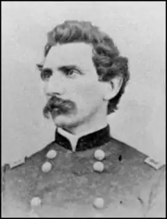 Black and white photo shows a man with wavy hair and a moustache. He wears a dark military uniform.