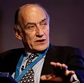 The head and shoulders of a white man in a dark suit and tie with dark, greying hair.