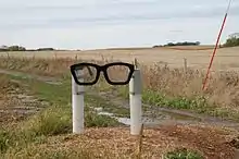 A sculpture consisting of two white posts holding a black spectacles frame in Buddy Holly's characteristic style