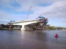 A T-shaped section of bridge being constructed over a river