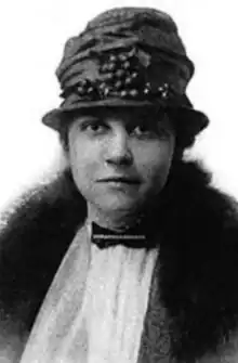 a black-and-white head-and-shoulders portrait of young white woman wearing a hat, a fur-collared coat, a white shirt, and a bow tie