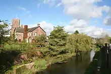 Water in front of trees, a house and a church.