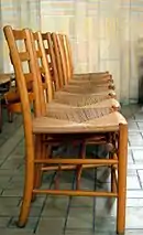  A row of brown, wooden chairs with a seat made of some woven material