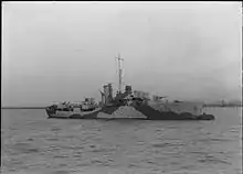 ship at sea steaming from left to right, her guns are unmanned and the bridge crew can be seen