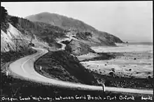 Black-and-white photograph of a narrow road winding around the cliffs overlooking the ocean.