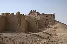 A ruinous stone wall with square bastions built of square stones leading up a hill