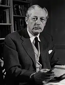 Harold Macmillan, wearing a jacket and tie, sitting at a desk