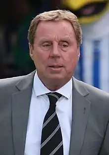 The upper body of a sandy haired man with a face with relaxed muscle tone. He is looking into the distance to his left. He is wearing a grey jacket and dark, striped tie.