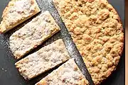 A round streuselkuchen, cut in pieces.  Half the cake has been dusted with powdered sugar