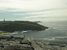 A rocky shoreline on a cloudy day. The outline of a building is just visible at left.