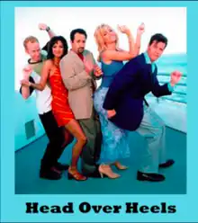 An image of multiple characters—three men and two women—as they pose in front of a blue/white background. The words "Head Over Heels" appear at the bottom of the image in black text. The image of the cast is in a blue frame.