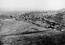 B&W photograph of a sprawling town of wooden buildings in a valley