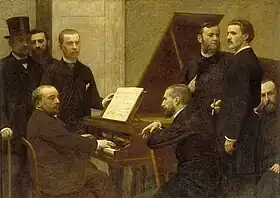 group of middle-aged men standing and sitting round a piano