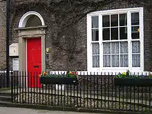 Colour photograph of the front of 23 Kirkgate in Thirsk. There are three storeys, two bay windows, and two stone steps leading to the entrance on left. This was the fictional Skeldale House in the James Herriot books and series. The building is now The World of James Herriot museum.