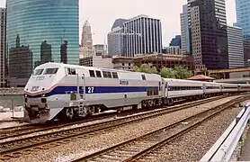 A light gray diesel locomotive with a blue stripe and two thinner red stripes on the side. The stripes narrow and angle downwards on the front.