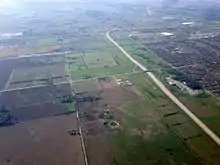 An aerial photograph of Highway 407 travelling north through farmland towards the interchange with Highway 401. Subdivisions of Mississauga are visible to the right.