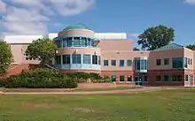 A beige building with a large windowed rotunda stands before a wide lawn.