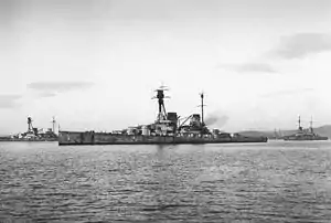 Side view of a large warship with a prominent tripod mast above the superstructure at anchor. Four gun turrets and two funnels are visible.