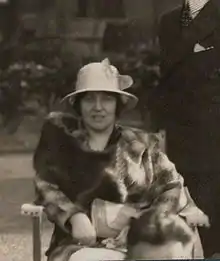 A finely-dressed woman in a white hat and fur coat