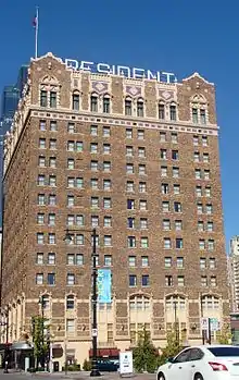 A 14-story brick building against a clear blue sky, seen from a block away. Its upper- and lowermost sections are ornate.