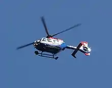 A blue and white painted helicopter flying in blue sky, pictured from below.