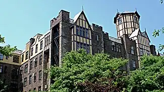 A brick and half-timber building rising several stories above some trees.