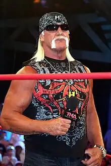 Hulk Hogan standing while holding a microphone, during a TNA Impact! taping