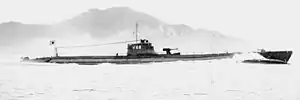 A World War II-era submarine in a body of water with a land mass in the background