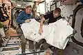 Anchored by their toes, Expedition 47 Commander Tim Kopra and Flight Engineer Tim Peake wrestle an M/D Cover Center Section into the vestibule while preparing for deberth of a Cygnus cargo vehicle from Node 1 (Unity).