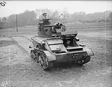 Photograph of a small tank with one soldier by the gun turret and another looking through an opening in the front