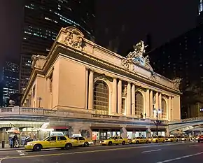 A row of yellow taxis in front of a multi-story ornate stone building with three huge arched windows.