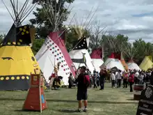 A row of several conical canvas dwellings, each decorated in traditional native themes, including animals and bright colours.