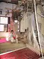 Boy next to two weaving looms with the weaving pattern on reams of paper (India).