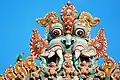 Thiruvanaikaval Kirtimukha top of gopuram with a ring-necked parakeet sitting next to it