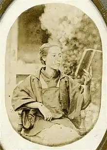 Monochrome photograph of an elderly Kusumoto Ine seated and reading a book