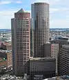 Aerial view of two skyscrapers; both have circular footprints and light red facades. The shorter of the two buildings, in the foreground, is topped by a pyramid-like cap, while the taller building has a flat roof.