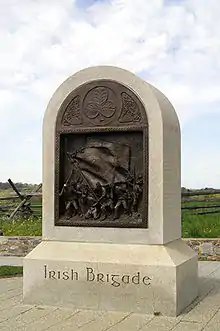 A tall stone monument with a rounded top and a bronze inset sculpture.  The base reads, Irish Brigade.