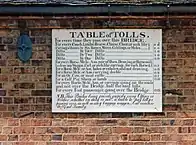 Antique table of bridge tolls now displayed on the outside of the toll house. Tolls range from a halfpenny for a pedestrian to two shillings for a large coach