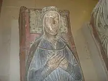 A photograph of a medieval tomb with a carving of Isabella on top. She is lying with her hands clasped, wearing a blue dress.