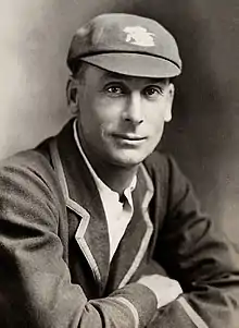 A black and white head and shoulders shot of a man wearing a cricket blazer and cap