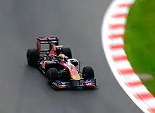 A navy blue and red Formula One car being driven at speed on a dry circuit