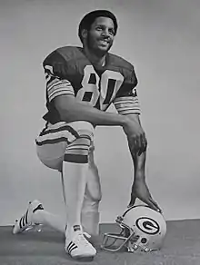 Black and white portrait of Lofton kneeling in his uniform