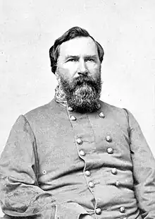 Black and white photo of a bearded man looking directly at the camera. He wears a gray military uniform with two rows of buttons.